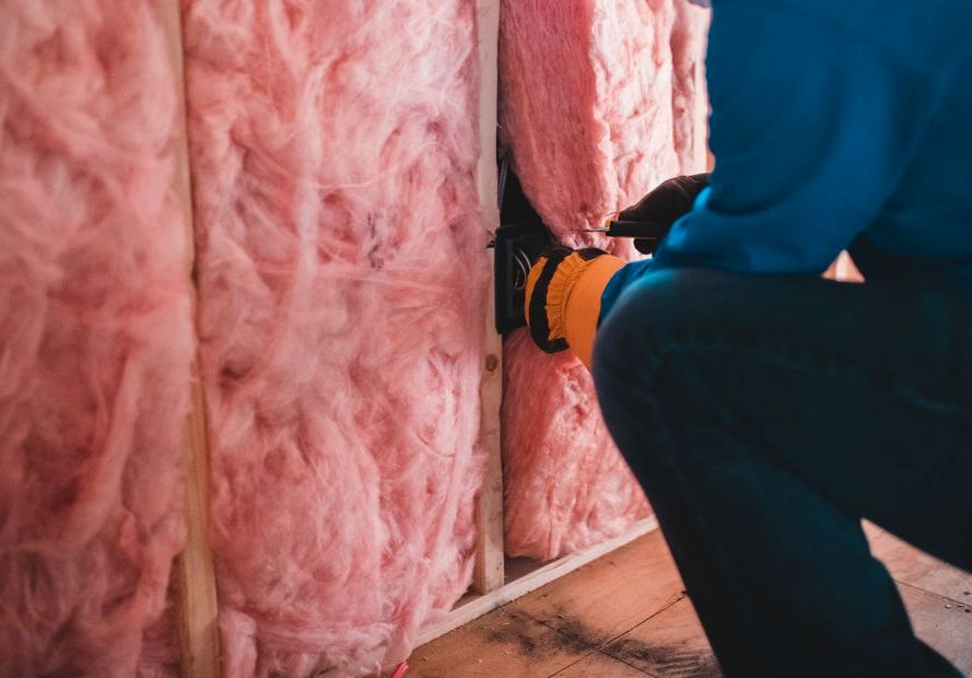 Crop unrecognizable worker in gloves sitting on haunches and insulating with pink stone wool